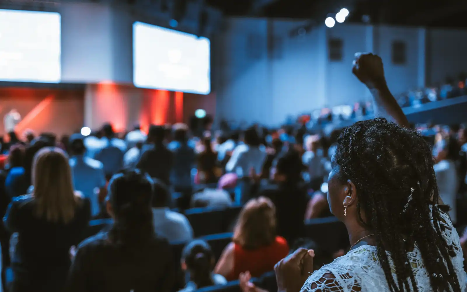 A woman in a large group of people raising her hand, representing getting found