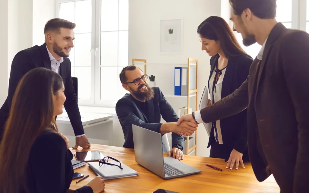 A group of professionals around a desk, smiling and shaking hands, representing success getting found online
